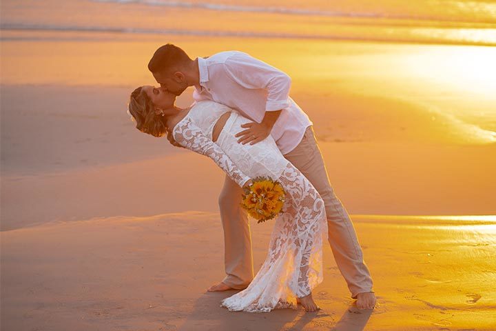 Casal de noivos se beijando na praia, em sessão de fotos após casamento