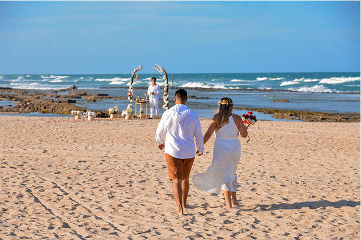 Homem e mulher caminhando na praia em direção ao altar para realizar renovação de Votos