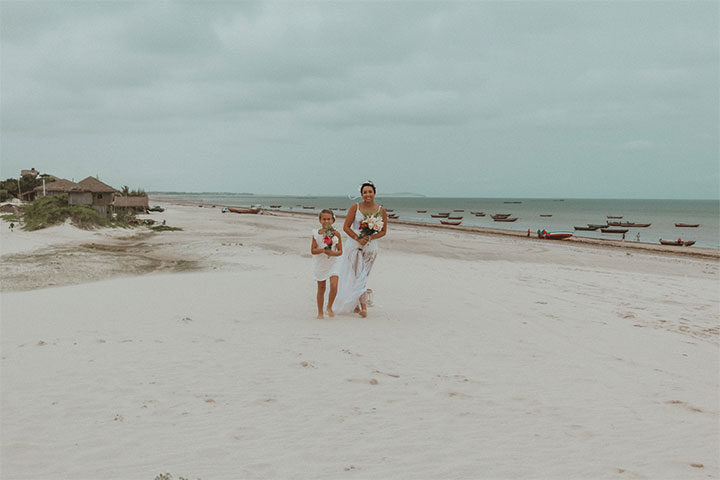 Mãe e filha segurando buquê de flores e caminhando na duna