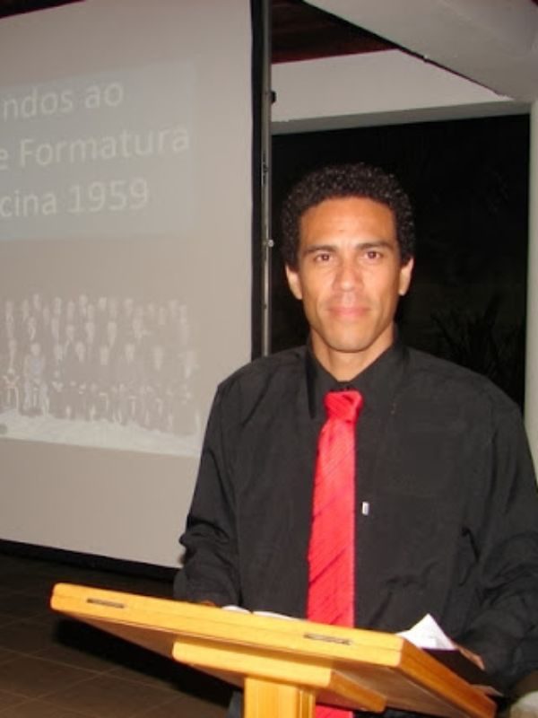 Homem vestindo roupa preta, gravata vermelha e em pé diante de púlpito em hotel